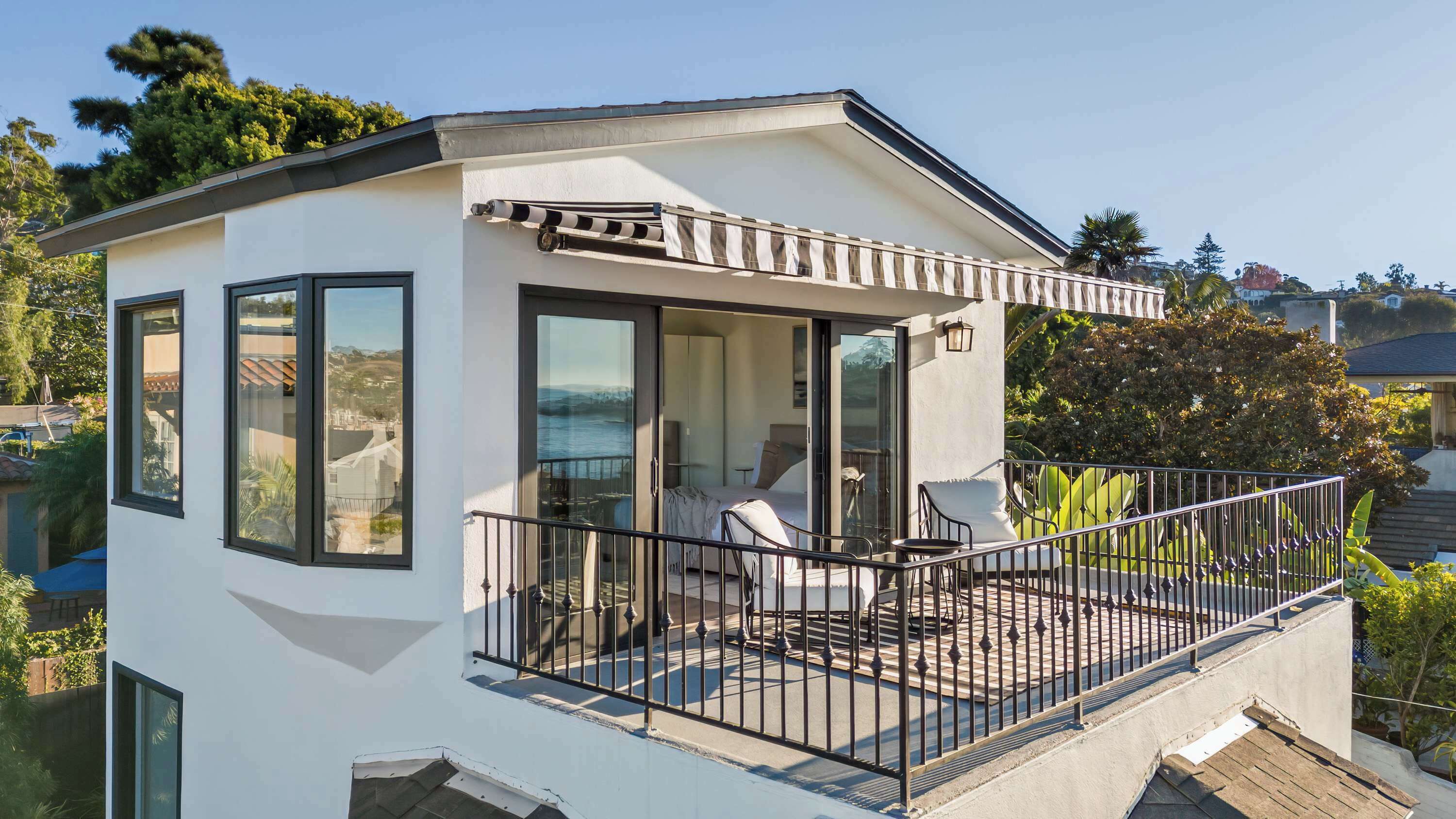 A modern two-story house with a balcony, large windows, and a view of the ocean.