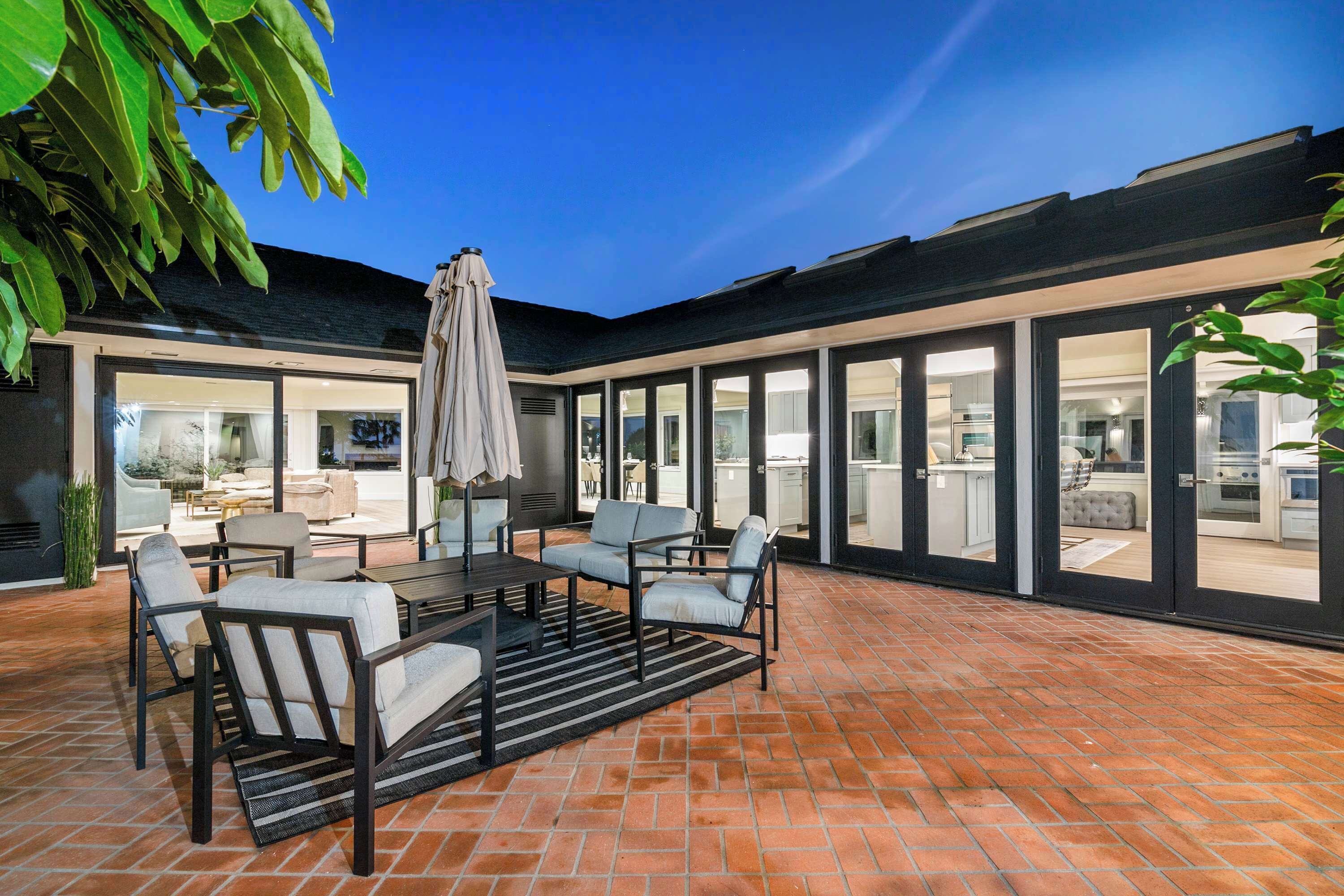A patio with a dining table and chairs, a large umbrella, and a brick floor.