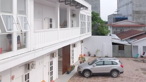 A white building with a balcony, a car parked in front, and a cobblestone street. - BI Hotel Kisaran (West Kisaran)