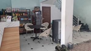 A small, well-lit room with a tiled floor, a wooden table, white chairs, a refrigerator, a door, and a staircase. - BI Hotel Kisaran (West Kisaran)