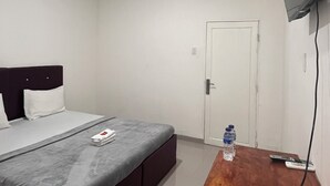 A hotel room with a bed, a wooden table, a TV mounted on the wall, and an air conditioning unit. - BI Hotel Kisaran (West Kisaran)