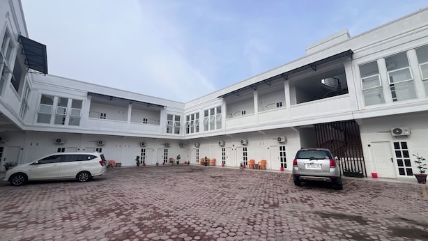A white multi-story building with a courtyard, air conditioning units, and a car parked in the driveway. - BI Hotel Kisaran (West Kisaran)