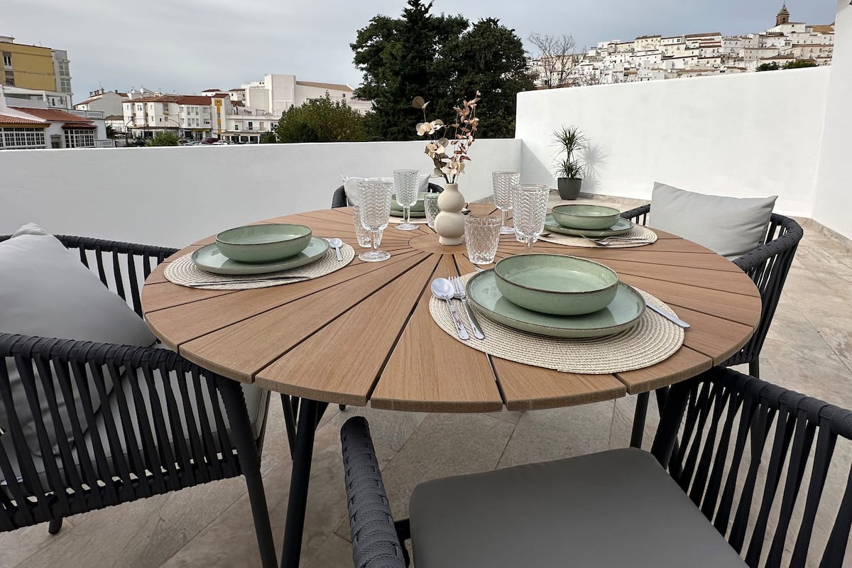 A round wooden table set for four with green plates, silverware, and clear glasses.