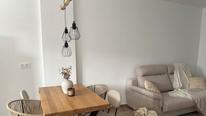 A modern living room with a wooden dining table, wicker chairs, a beige sofa, and a hanging light fixture. - Casa rural Los Alcornocales (Alcala de los Gazules)