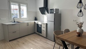 A modern kitchen with a built-in oven, microwave, and coffee maker. There is a dining table with chairs and a vase with flowers. - Casa rural Los Alcornocales (Alcala de los Gazules)