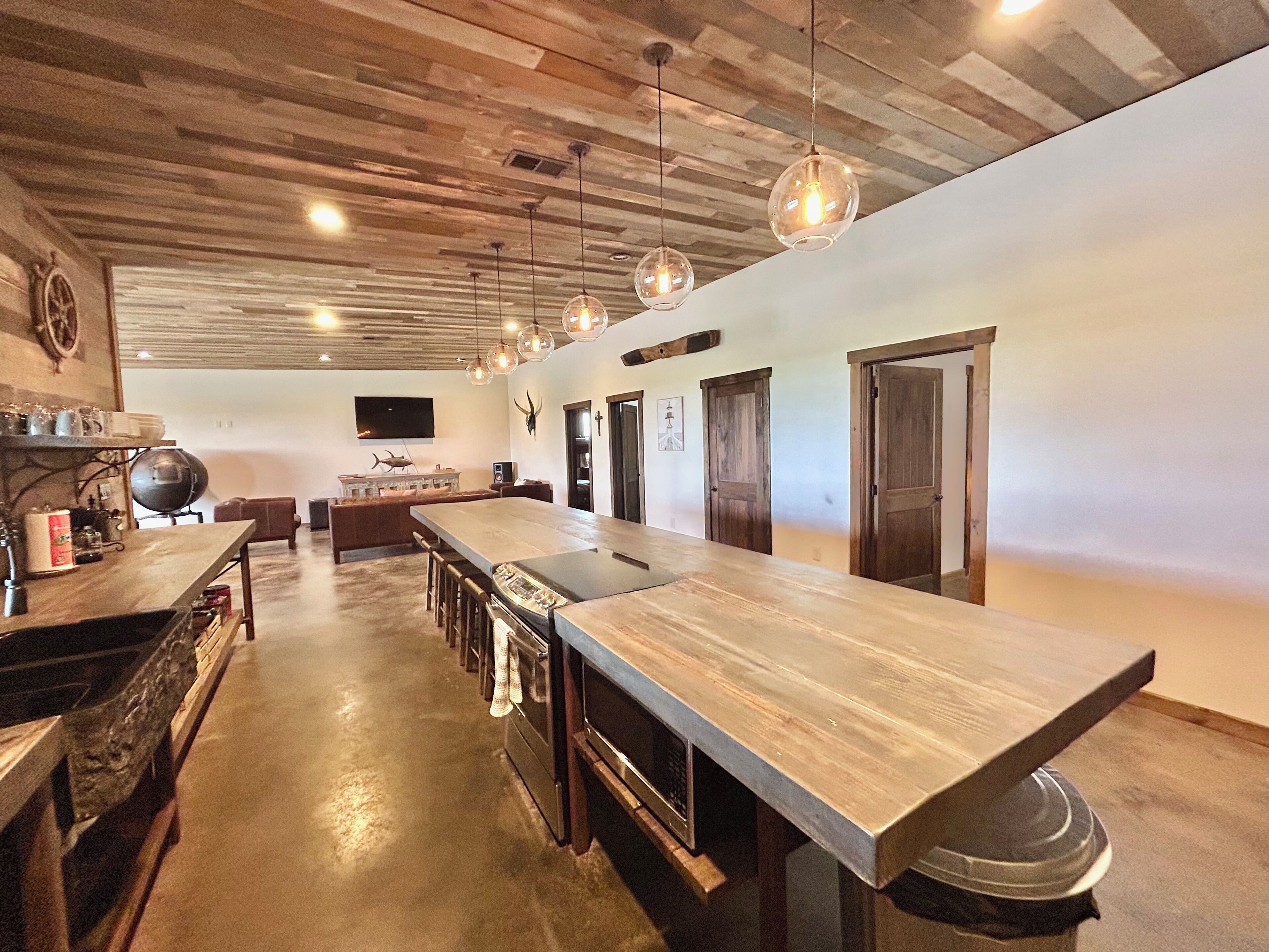 A spacious kitchen with a long counter, hanging pendant lights, and a rustic wooden ceiling.