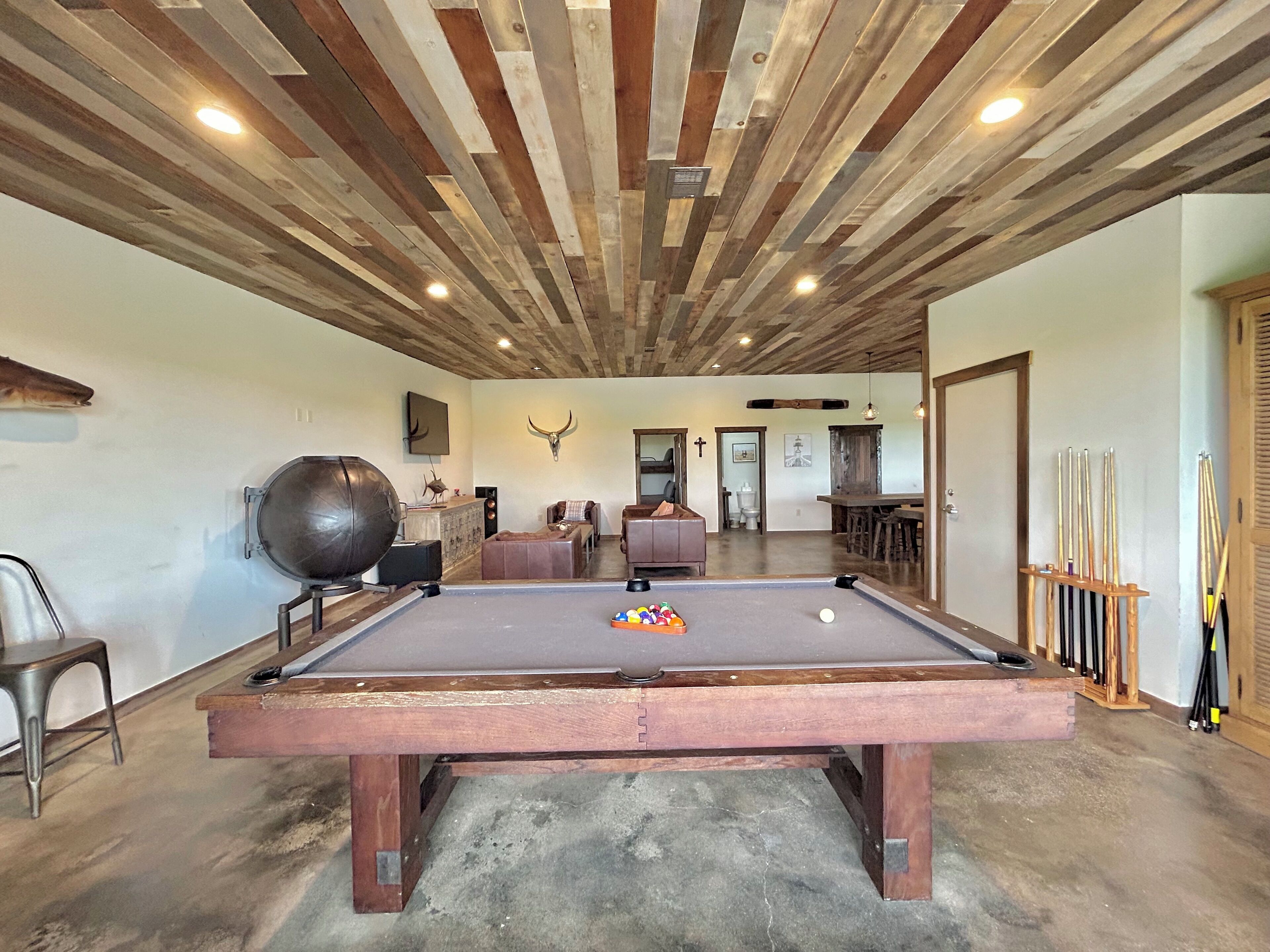 Une table de billard dans une pièce avec un plafond en bois, une décoration murale représentant une tête de taureau et un porte-billes.