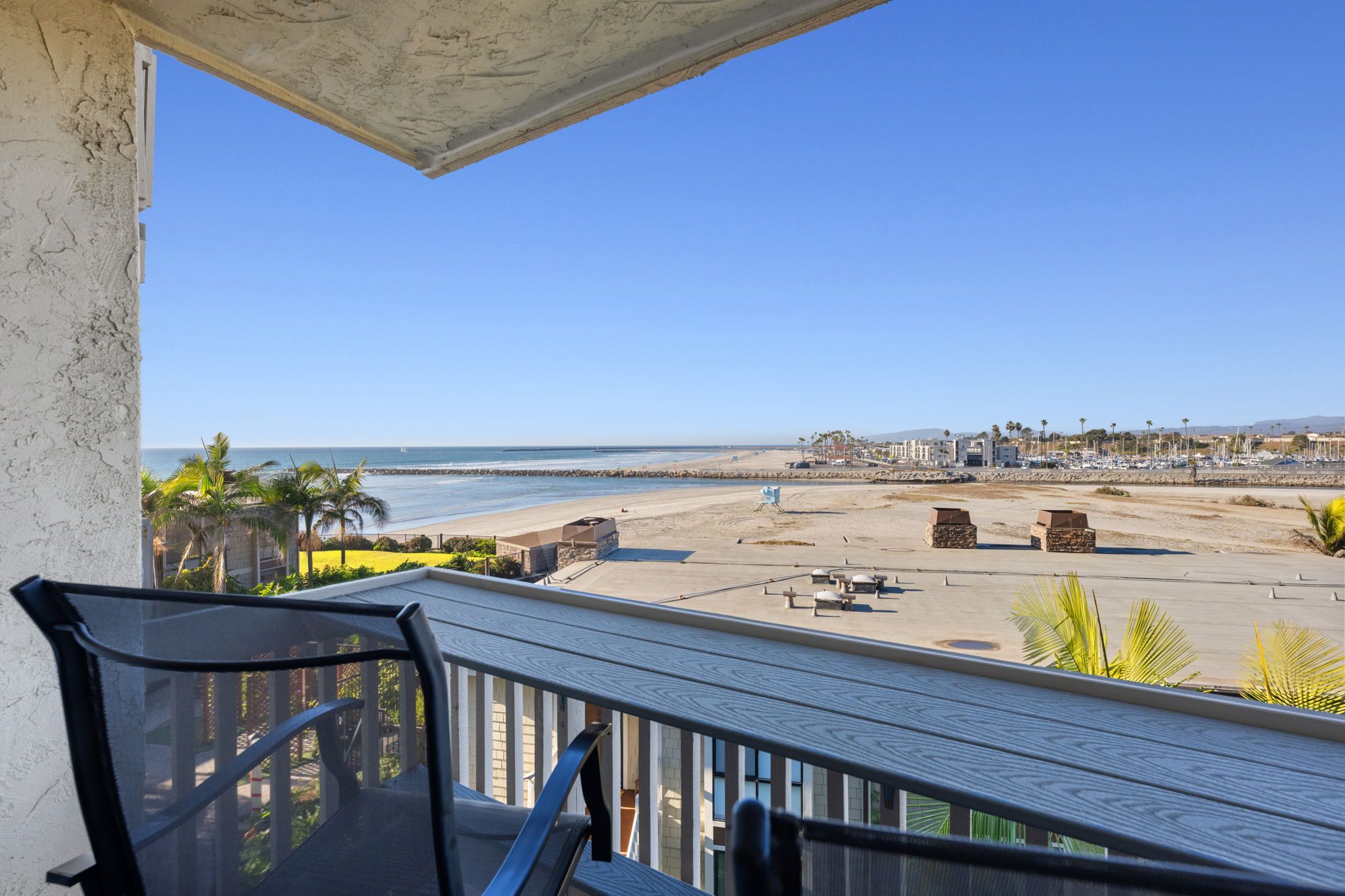Un balcon avec vue sur une plage, un ciel dégagé et un paysage urbain lointain.