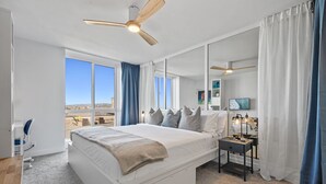 Une chambre à coucher avec un grand lit, un bureau, une chaise, une table de chevet avec une lampe et un ventilateur de plafond.