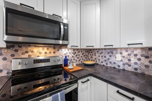 Une cuisine équipée d’un four à micro-ondes, d’un four et d’une cuisinière en acier inoxydable, de meubles blancs et d’un crédence décorée.