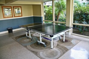 Mesa de ping pong en una habitación con vistas a la vegetación a través de amplias ventanas.