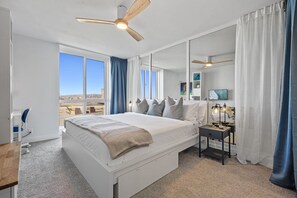 A modern hotel room with a large bed, two ceiling fans, a TV, and a view of the cityscape. - *New Listing* Beautiful remodeled unit - with stunning ocean views -  E209 North Coast Village (Oceanside)