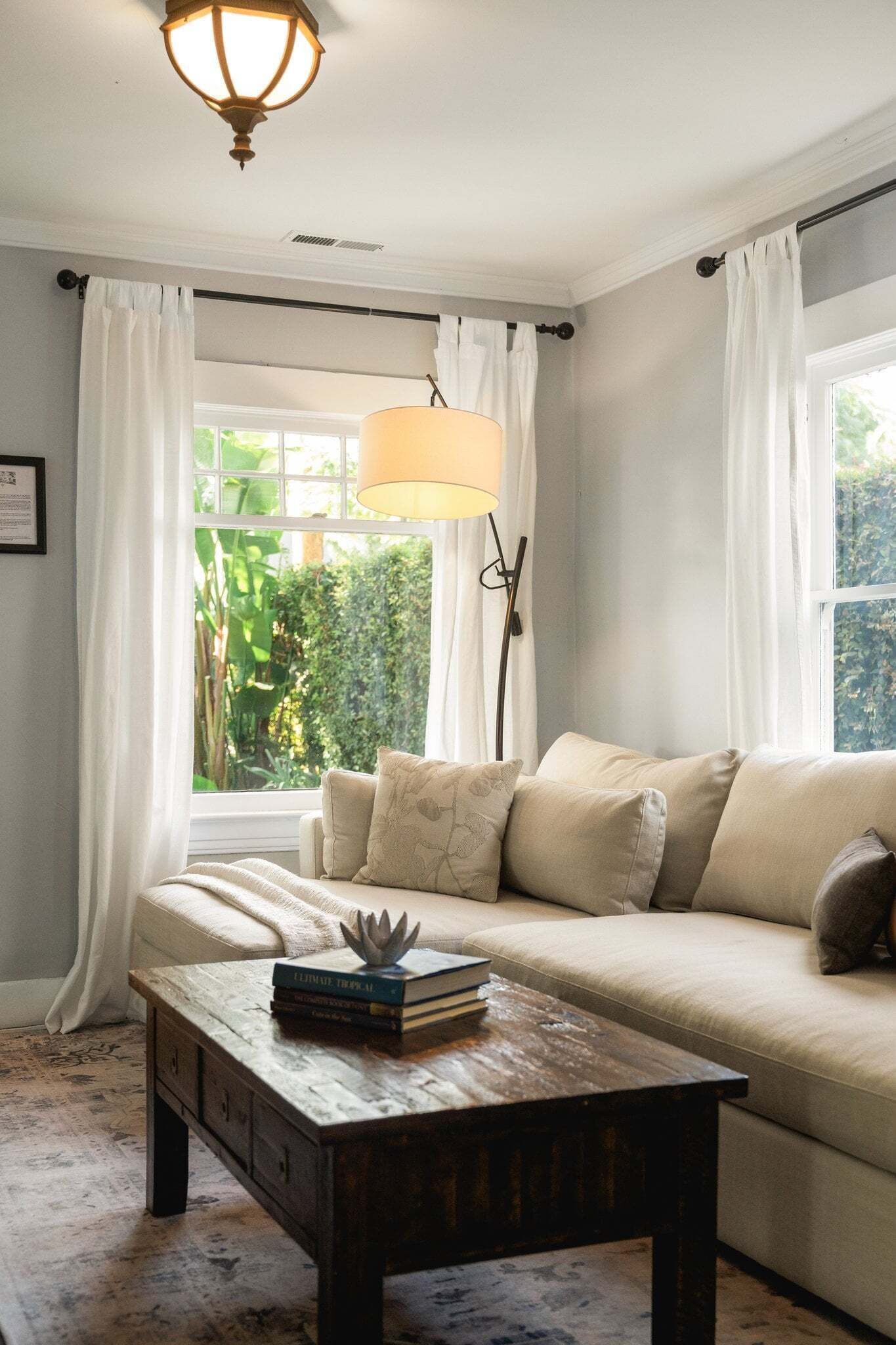 Una habitación con sofá, una mesa con libros, una lámpara y una ventana con cortinas.
