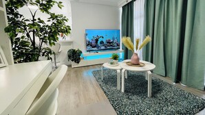 Un salon moderne doté d’un téléviseur à écran plat, d’un ventilateur de plafond et d’un grand rideau vert.