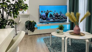 Un salon moderne doté d’un grand téléviseur à écran plat, d’un canapé blanc, d’une table basse et de plantes décoratives.