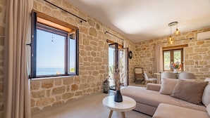 Una habitación con paredes de piedra, un sofá, una mesa redonda y vista al mar.