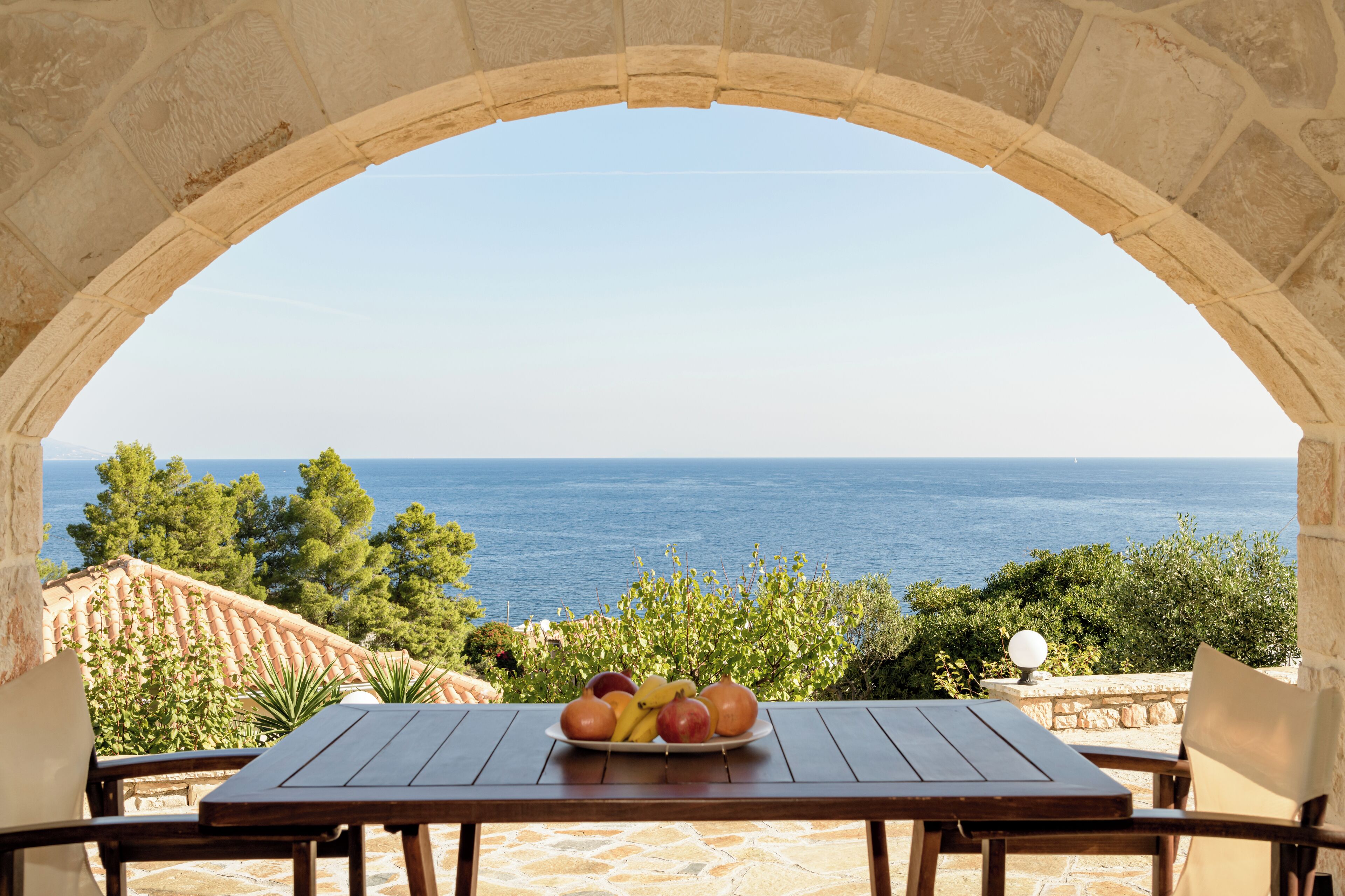 Une table avec une assiette de fruits et une vue sur la mer, visible à travers une arche.
