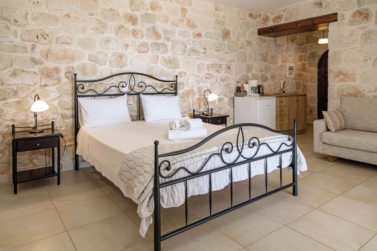 A bedroom with a stone wall, a bed with a metal frame, two bedside tables with lamps, a wooden cabinet, and a sofa.