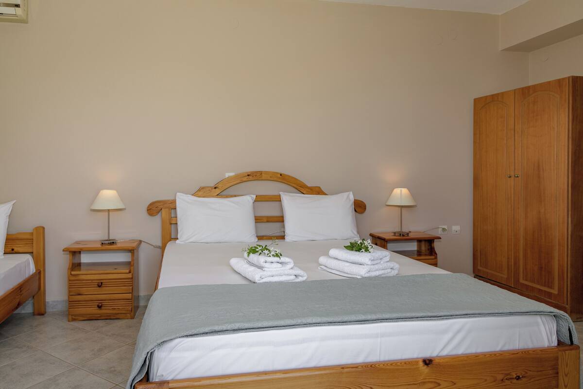 A neatly arranged bedroom with a wooden bed, two bedside tables with lamps, a wardrobe, and neatly folded towels on the bed.