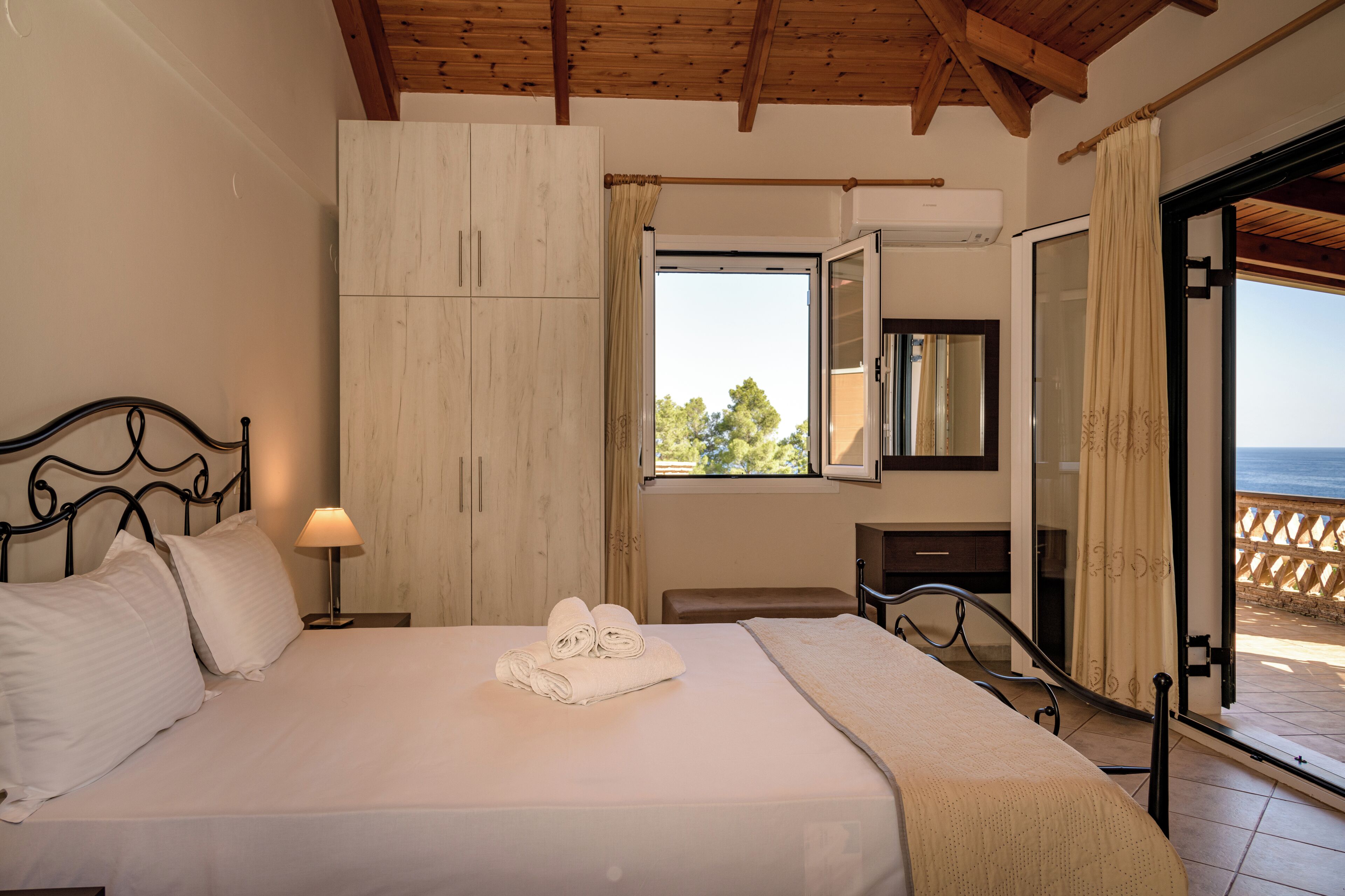 A bedroom with a bed, a nightstand, a wardrobe, a window with a view, and a balcony.