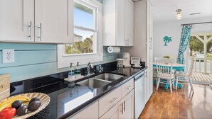 Una cocina con armarios blancos, encimera negra, un lavabo y una ventana.