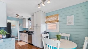 Una cocina con armarios blancos, una mesa de comedor con sillas blancas y una pared azul.