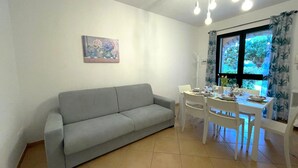 Una sala de estar con un sofá gris, una mesa de comedor preparada para cuatro personas y un cuadro en la pared.