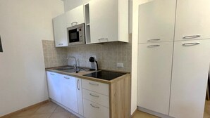 Una cocina con gabinetes blancos, microondas, lavamanos y cafetera.