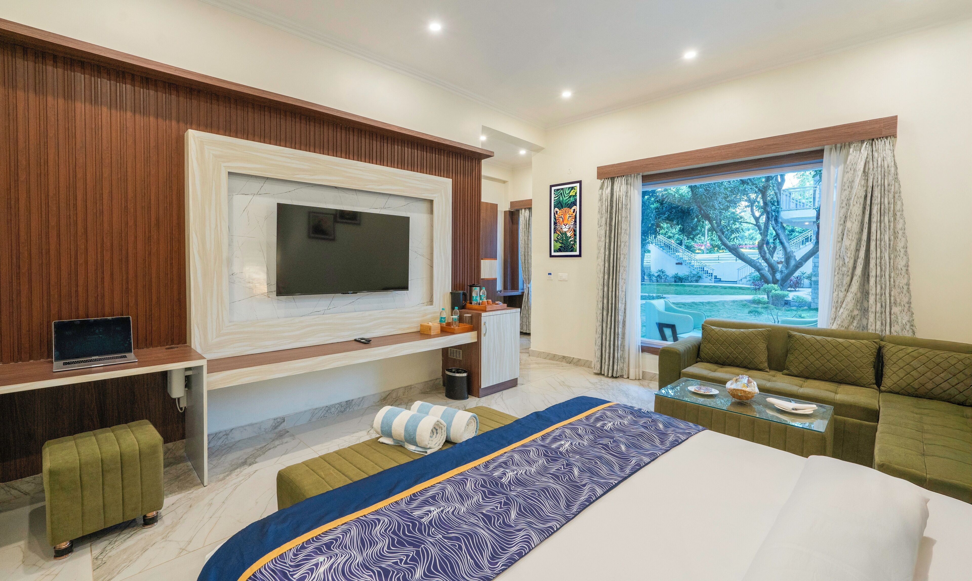 Quarto de hotel moderno com uma televisão grande, um sofá, uma mesa pequena e vista para o exterior.