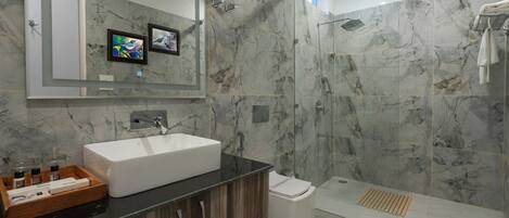 Un baño moderno con un lavabo blanco grande, una ducha con puerta de cristal y paredes de mármol.