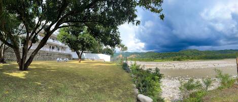 A grassy area with a building, a river, and a mountainous backdrop.