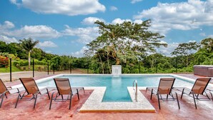 Una piscina con sillas de descanso y un jacuzzi, rodeada de follaje y árboles.