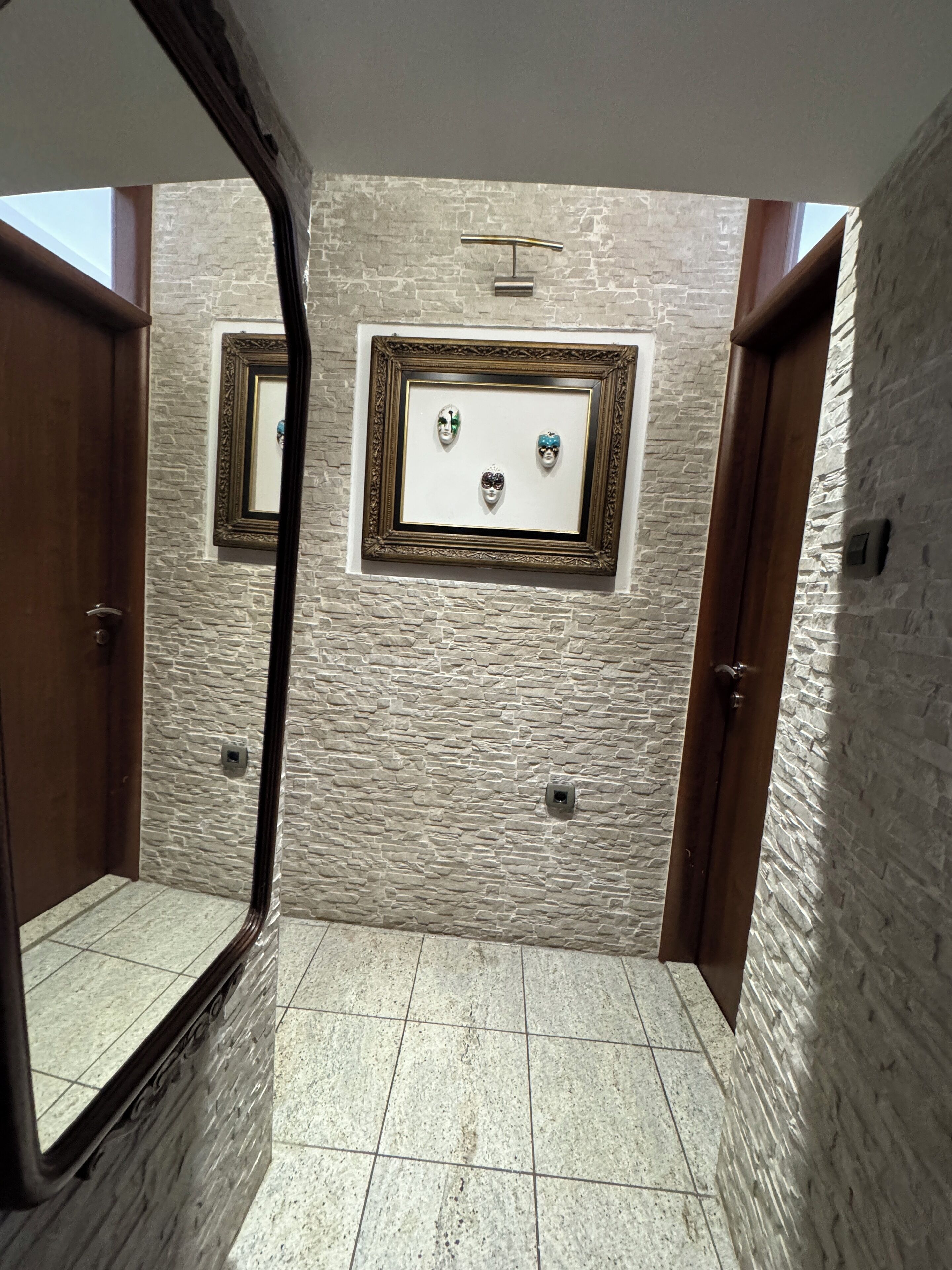 Un baño con pared de piedra, un espejo enmarco y piso de baldosas.