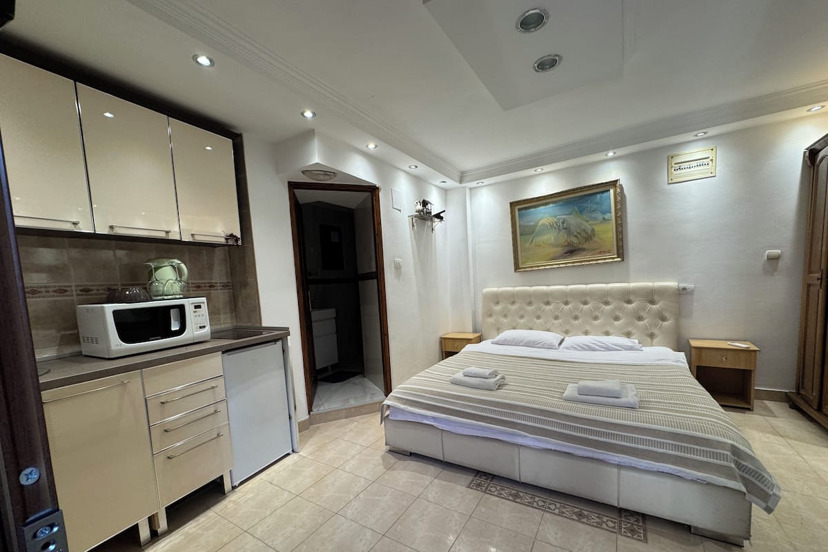 A bedroom with a bed, bedside tables, a microwave, and a bathroom door.