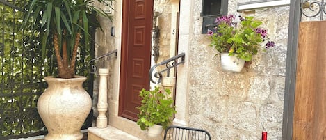 A stone building with a red door, a potted plant, a table with a bottle and glasses, and a number sign.