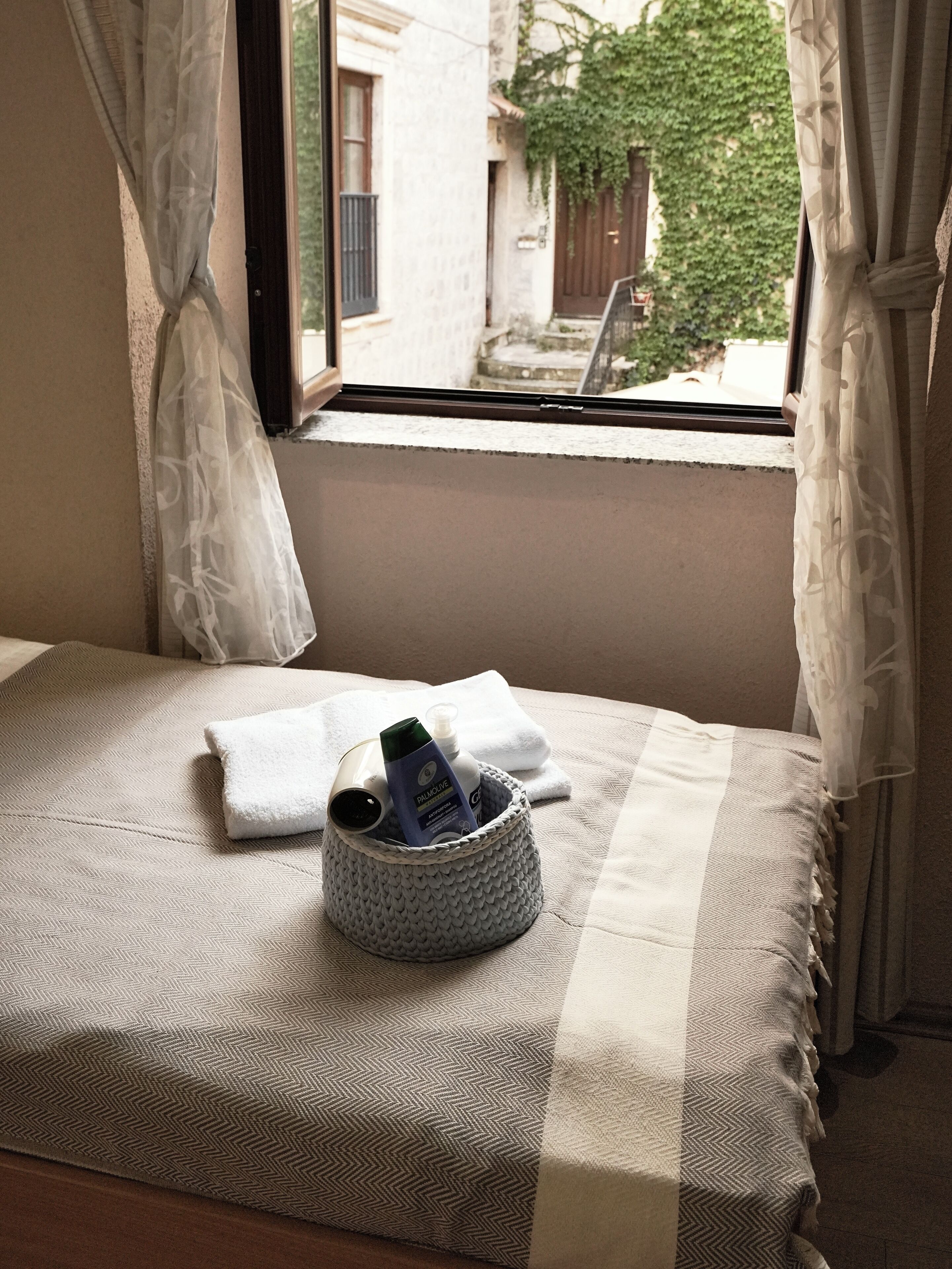 A bed with a herringbone-patterned bedspread, a white towel, and a basket containing toiletries.
