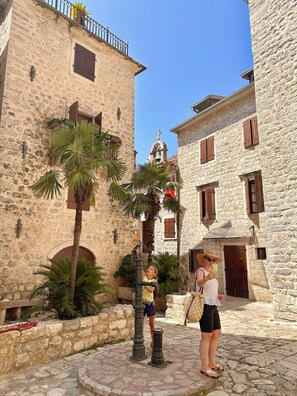 A stone building with a bell tower, palm trees, and a cobblestone courtyard. - Vita Mundo (Kotor)