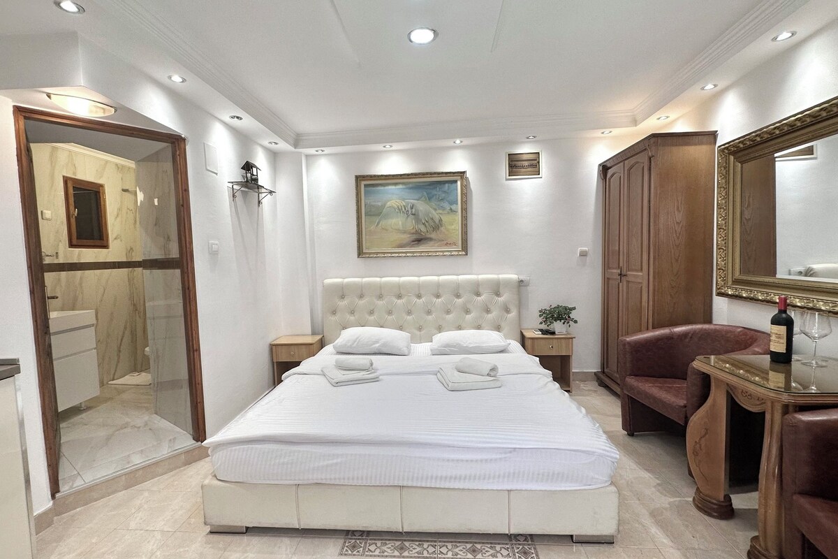 Un dormitorio con una cama grande, una mesita de noche, una silla, un armario de madera, un espejo y un cuadro en la pared.