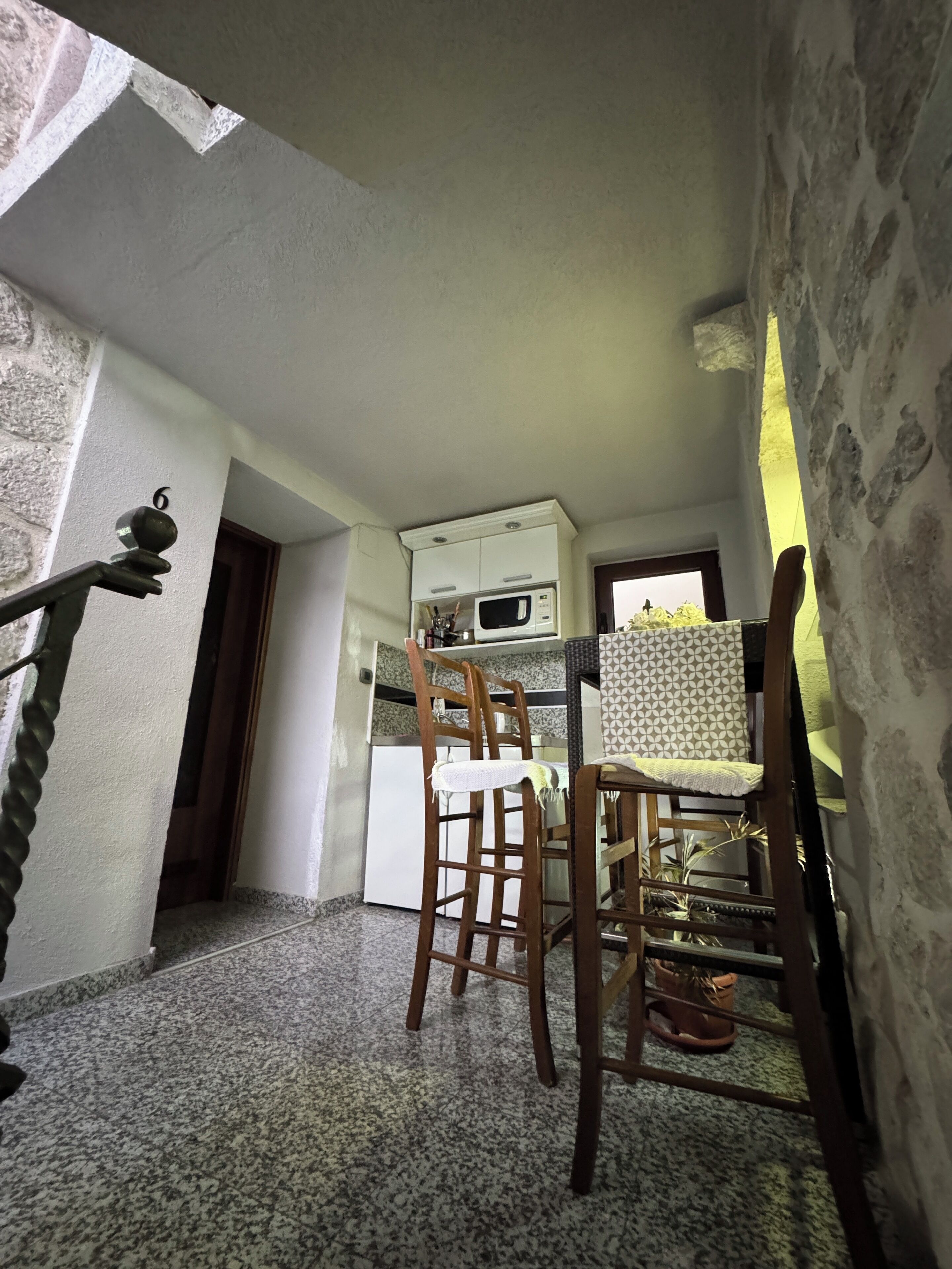 A narrow kitchen with a microwave, a wooden chair, and a small table.