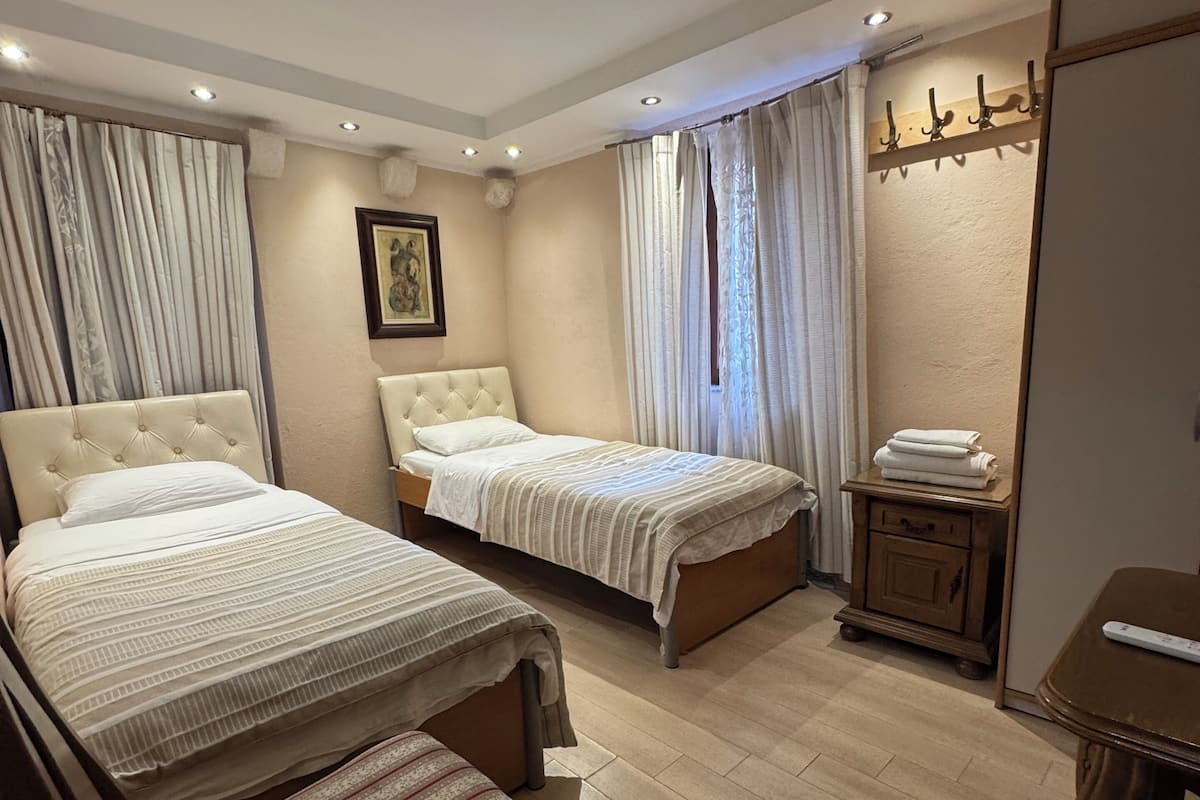 A hotel room with two beds, a wooden bench, a small table, a coat rack, and a ceiling light.