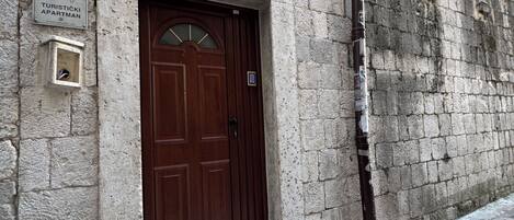 A stone building with a wooden door, a small sign above the door, and a window with a view of the sky.