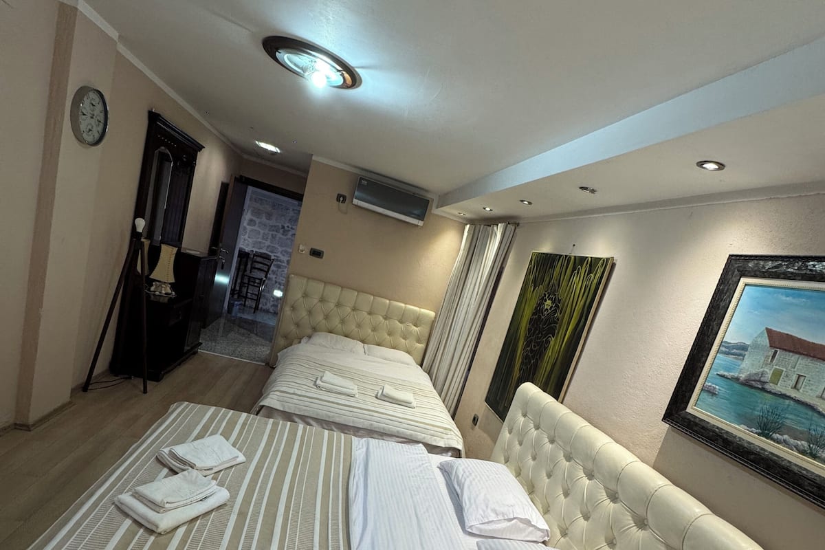 A hotel room with a large bed, a wall clock, an air conditioning unit, and a painting.
