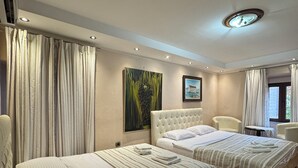 Una camera d'albergo con due letti, un'ampia finestra con tende, un quadro appeso al muro e una luce a soffitto.