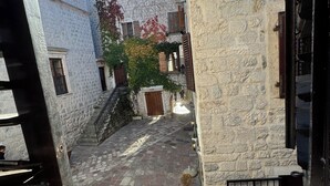 Un cortile in pietra stretto con una scala in legno, piante in vaso e vista su un edificio con una torre.