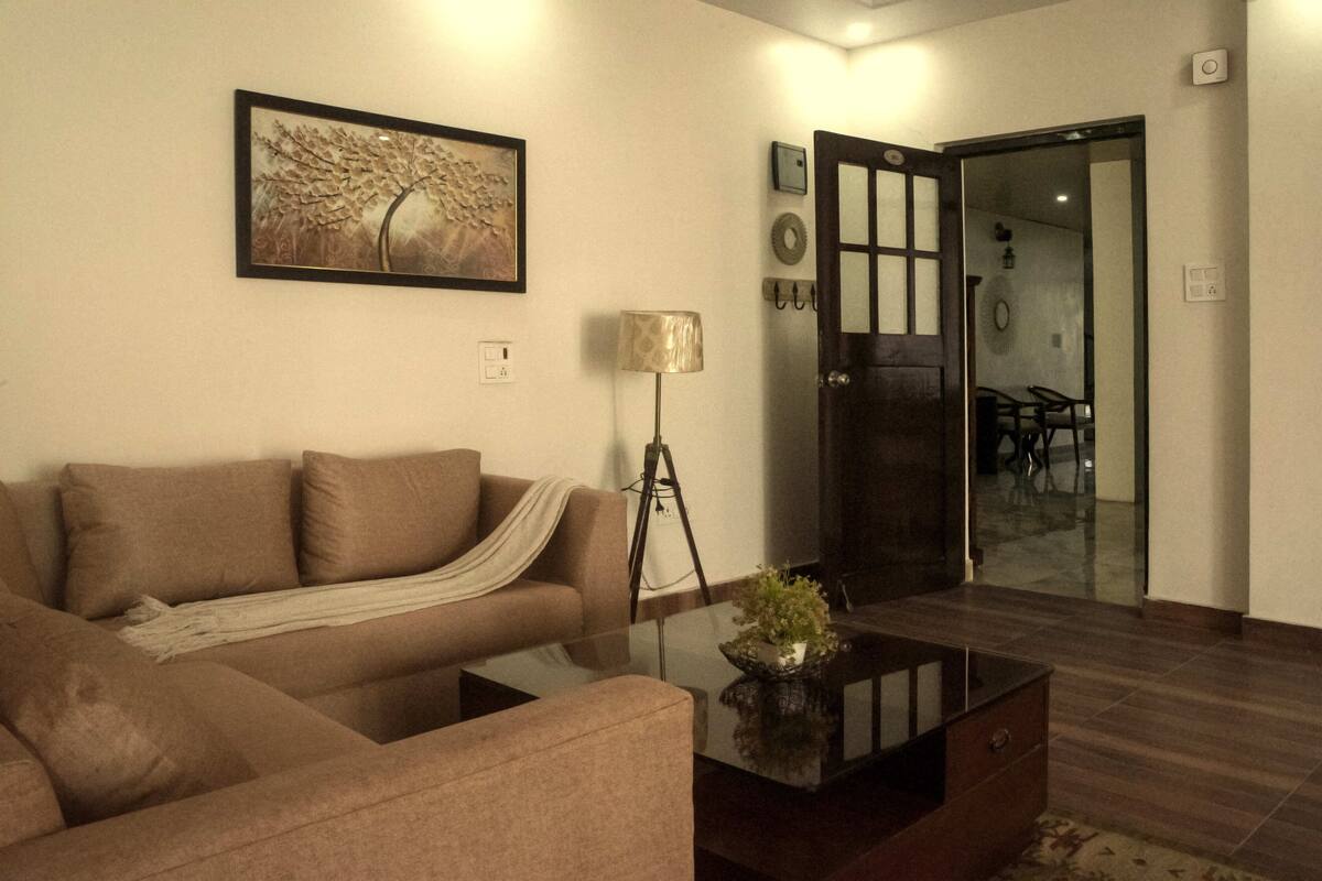 Una sala de estar con un sofá, una mesa de centro con una planta, una lámpara y un cuadro en la pared.