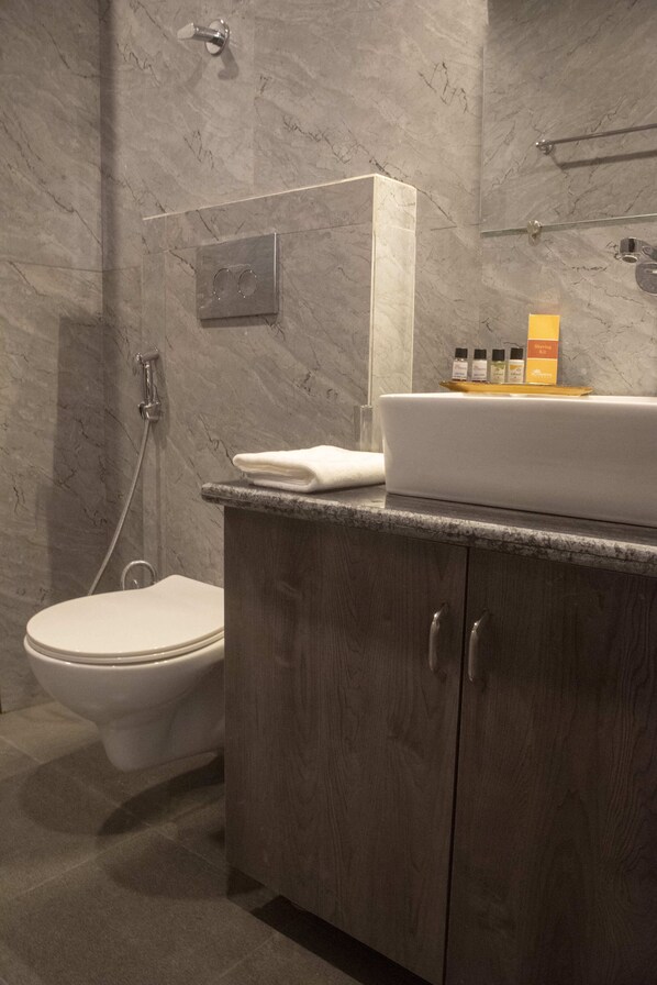 A modern bathroom with a marble wall, a white toilet, a wooden vanity with a sink, and a glass shower enclosure.