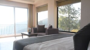 Een hotelkamer met een groot bed, een slaapbank, een kleintje tafeltje en uitzicht op het omliggende landschap door grote ramen.