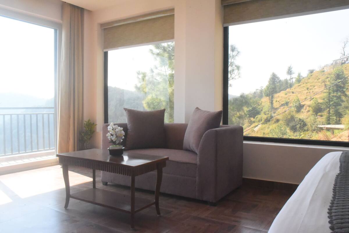 Una sala de estar moderna con un sofá, una mesa de centro de madera y vistas a un paisaje montañoso a través de grandes ventanales.