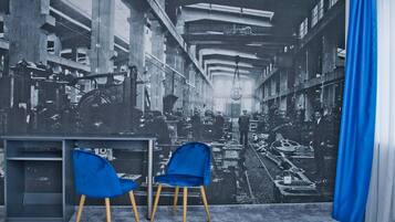 Una habitación con un gran mural de una escena industrial, dos sillas azules y una cortina azul.