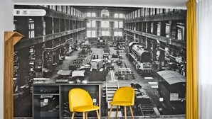A room with a large black and white industrial-themed mural on the wall, two yellow chairs, and a wooden sideboard. - ParkApartamenty (Chrzanow)